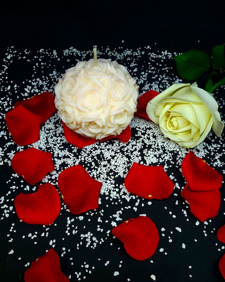 Bougie boule de roses en cire de coco, posée au centre de pétales de rose rouges.
